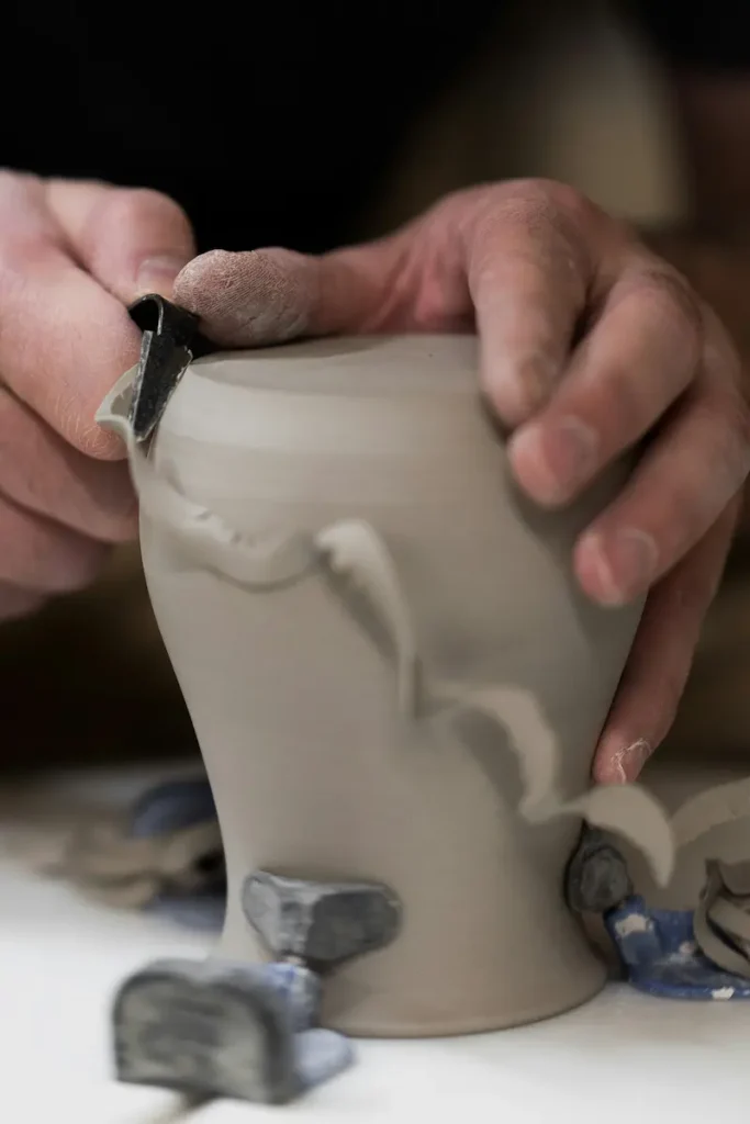 Unas manos dándole forma a un trozo de barro con un utensilio.